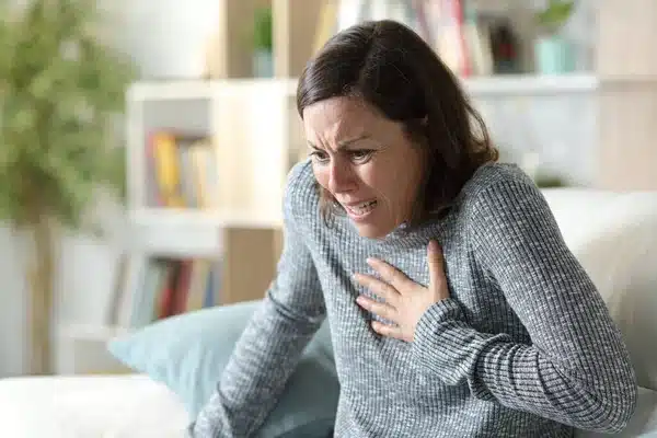 Mid-age women touching her chest while sitting on the sofa.
